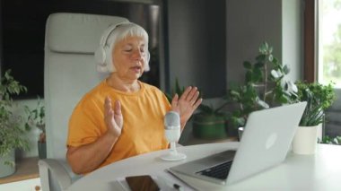 Gülümseyen profesyonel 50 'ler kadın podcaster' ı ev stüdyosundan podcast yapıyor. Evden çalışan bir kadın podcast kaydediyor.