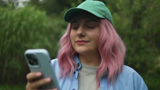 白种人年轻漂亮的粉红头发女人 头戴绿帽的送货员走在街上 用手机在户外拍摄高质量的Fullhd镜头 — 图库视频影像