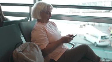 Havaalanındaki son sınıf beyaz kadın uçuş biletini beklerken akıllı telefonunu kontrol ediyor.