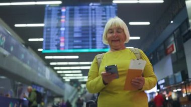 Havaalanı terminalinde, son sınıf sarışın, 50 'li yaşlarda, bavullu bir kadın. Kadın kameraya gülümsüyor. Yüksek kaliteli FullHD görüntüler. O ayakta duruyor ve bagaj taşıyor. Seyahat Konsepti