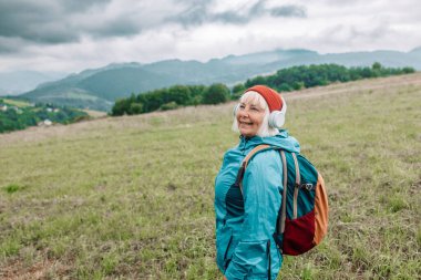 Açık havada müzik dinleyen ve doğa güzelliğinden esinlenerek manzaraya hayran olan mutlu, aktif, yaşlı turist kadın. Yüksek kalite fotoğraf