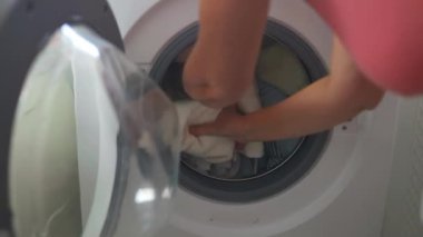 Beyaz, son sınıf öğrencisi kadın kirli çamaşırları çamaşır makinesine koydu. Mutlu kız çamaşır makinesinin önünde oturuyor, evde bir sürü kirli çamaşır var. Yüksek kaliteli FullHD görüntüler