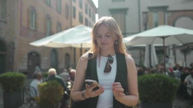 Bergamo Avrupa İtalya, yaz tatili turizminde seyahat eder. Elinde cep telefonu kamerasıyla tepede dikilmiş etrafa bakan gülümseyen genç kız. Yüksek kaliteli FullHD görüntüler