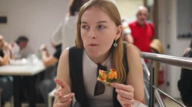 Güzel, gülümseyen, sarışın bir kız bir kafede yemek yiyor, masada oturuyor ve İtalyan pizzası yiyor. Reklam, ticari tasarım. Yüksek kaliteli FullHD görüntüler