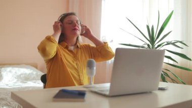 Dizüstü bilgisayarında kulaklıklar ve mikroskopla podcast yapan bir kadın. Kadın podcaster kendi stüdyosundan ses yayını yapıyor. Yüksek kaliteli FullHD görüntüler