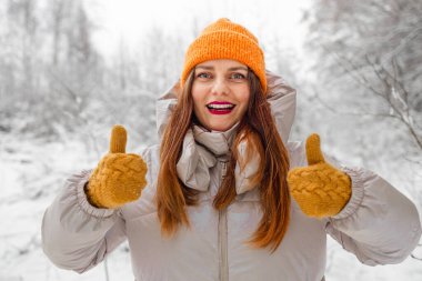 Mutlu, güzel bir kızın portresi, neşeli, pozitif bir kadın şarkı söylüyor, karla oynuyor, kar taneleriyle oynuyor, kış kıyafetleriyle dışarıda eğleniyor, şapka takıyor, gülümsüyor. Kış mevsimi, hava. Yüksek