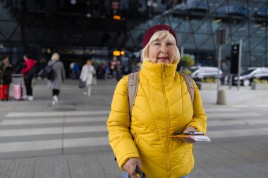 Modern havaalanı terminalinin yanındaki modern nakliye durağında elinde bavulla yürüyen 60 'lı yılların çekici, çekici bayan yolcusu. Tatiller, seyahat ve aktif yaşam tarzı kavramı 