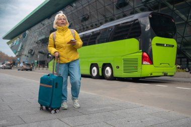 Turist taksi bekliyor. Kıdemli kadın havaalanının dışında durur ve tatilden sonra taksi bekler ya da seyahat eder. Kadın turist eve geldi. Yüksek kalite fotoğraf