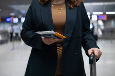 Elinde bavul, pasaport ve biletle akıllı telefondan yazan, tren istasyonunda ya da havaalanında ulaşımı bekleyen beyaz bir iş kadını. Seyahat ve cihaz, seyahat uygulaması, kapatın. Yüksek