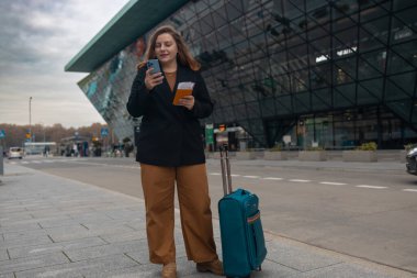 Havaalanından aceleyle çıkan bir iş kadını, elinde biletlerle şehir caddesinde duruyor ve bir bavul taşıyor. Havaalanında taksi bekliyorum. Cep telefonuyla taksi çağırma fikri. Yüksek