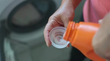 Kadın plastik kapağa sıvı çamaşır jeli döküyor çelik renkli çamaşır makinesinin arka planına karşı. Bir kız çamaşırları düzleştirmek için şeffaf bir kremi dikkatlice doldurur. Yüksek kalite