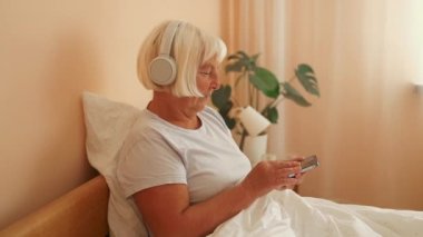 Evde kulaklıkla müzik dinleyen 60 'lı yaşlardaki rahat bir kadın. Yüksek kalite Tam HD görüntü