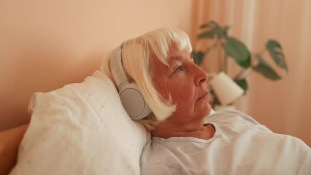 放宽了60多岁的老年妇女在家用耳机听音乐 优质全息高清影片 — 图库视频影像