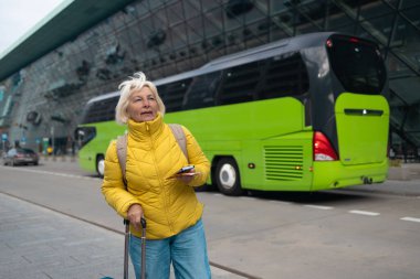 Turist taksi bekliyor. Kıdemli kadın havaalanının dışında durur ve tatilden sonra taksi bekler ya da seyahat eder. Kadın turist eve geldi. Yüksek kalite fotoğraf