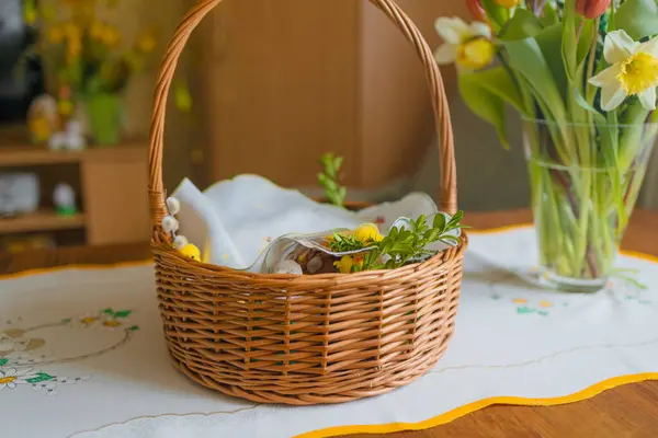 Traditional Easter basket on family table in Poland. Easter modern eggs, easter bread, ham, beets, butter, in wicker basket decorated with green boxwood branches and flowers on rustic wooden table