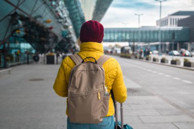Modern havaalanı terminalinin yanındaki modern nakliye durağında elinde bavulla yürüyen 60 'lı yılların çekici, çekici bayan yolcusu. Tatiller, seyahat ve aktif yaşam tarzı kavramı 
