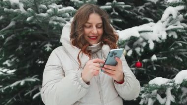 Karlı bir kış parkında cep telefonunu kullanan genç ve güzel bir kadın. Soğuk kış mevsiminde kadınların haberlere bakması ve dışarıda cep telefonuyla mesajlaşması.. 