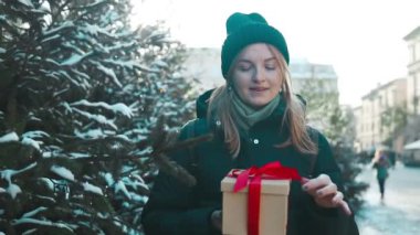 Noel pazarında elinde Noel hediyesi kutusuyla mutlu, genç ve çekici bir kadın. Neşeli güzel kız hediye kutusunu elinde tutuyor. Kış tatili indirimi. Yüksek kaliteli FullHD görüntüler