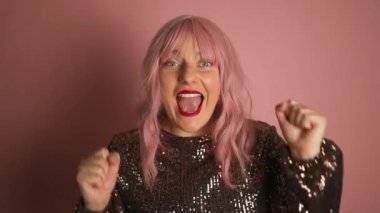 Genç, parlak elbiseli pembe saçlı kadının kameraya bakarken pembe arka planda yalnız durmasına şaşırdı. Yüksek kaliteli FullHD görüntüler