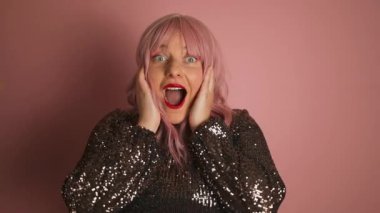 Genç, parlak elbiseli pembe saçlı kadının kameraya bakarken pembe arka planda yalnız durmasına şaşırdı. Yüksek kaliteli FullHD görüntüler