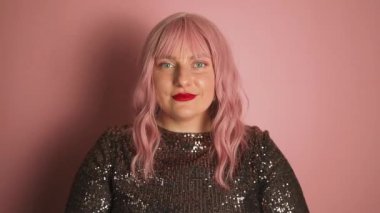 Elbise giymiş güzel beyaz kadın portresi kalp şeklinde el hareketleriyle pembe arka planda poz veriyor. Sevgililer Günü. Yüksek kaliteli FullHD görüntüler