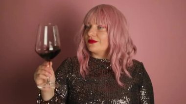 Parlak, modaya uygun, siyah elbiseli, elinde şarap kadehi olan ve pembe arka planda içki içen zarif, pembe saçlı kadın. Doğum gününü kutlayan bir kadın..