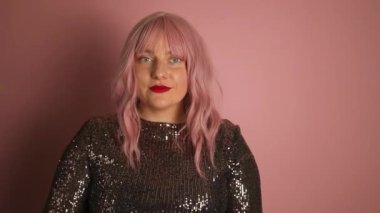 Genç, mutlu, neşeli, neşeli, başarılı Avrupalı, zarif bir elbise giyen, bir şeyi gösteren, gülümseyen ve pembe arka planda kendine güvenen bir kadın. 