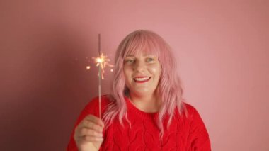 Güzel pembe saçlı kadın parlak makyajlı kırmızı ruj örülmüş kırmızı kış süveteri içinde el bengal ışığı tutuyor. Yılbaşı tatili, yeni yılı kutluyoruz. Yüksek kaliteli FullHD görüntüler
