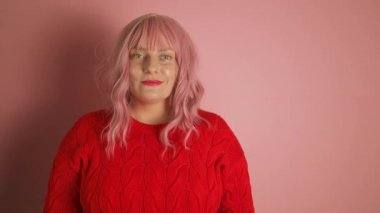 Genç, mutlu, neşeli, neşeli, başarılı, kırmızı kazaklı, bir şeye işaret eden, gülümseyen ve pembe arka planda kendinden emin görünen Avrupalı kadın. 