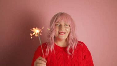 Güzel pembe saçlı kadın parlak makyajlı kırmızı ruj örülmüş kırmızı kış süveteri içinde el bengal ışığı tutuyor. Yılbaşı tatili, yeni yılı kutluyoruz. Yüksek kaliteli FullHD görüntüler