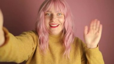 Mutlu beyaz kadın cep telefonuyla video görüşmesi yapıyor. Parlak pembe arka planda el ele selamlaşmalar, stüdyo portresi. Yüksek kaliteli FullHD görüntüler