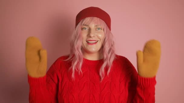 幸せな若いピンクの髪のヨーロッパの女性は ピンクの背景に何かを指す赤いセーターで振動腕を楽しんでいます 高品質のフルHd映像 — ストック動画