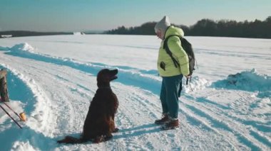 50 'li yaşlardaki mutlu güzel kadın kış tatilinde kış karının tadını çıkaran köpeğine kar taneleri üflüyor. İnsanlar ve hayvanlar birlikte eğleniyor ve gülümsüyor.