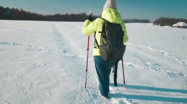Sırt çantalı ve kar ayakkabılı yaşlı kadın yürüyüşçü, soğuk havada kış ormanlarında karla kaplı yolda yürümeyi sever. Kış sporu aktivitesi. Yüksek kaliteli FullHD görüntüler