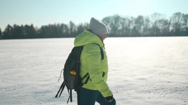 Sırt çantalı ve kar ayakkabılı yaşlı kadın yürüyüşçü, soğuk havada kış ormanlarında karla kaplı yolda yürümeyi sever. Kış sporu aktivitesi. Yüksek kaliteli FullHD görüntüler