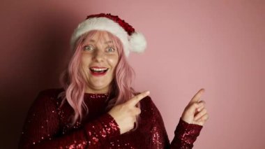 Genç, mutlu, neşeli, neşeli, başarılı Avrupalı, zarif bir elbise giyen, bir şeyi gösteren, gülümseyen ve pembe arka planda kendine güvenen bir kadın. 