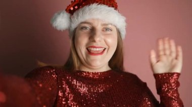 Mutlu, genç, güzel, Noel Baba şapkalı kadın cep telefonu uygulamalarını kullanarak video görüşmesi yapıyor, sosyal ağda online video kaydediyor ya da 2024 yılbaşı veya Noel 'de dilekleri okuyor. Yüksek