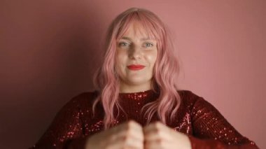 Elbise giymiş güzel beyaz kadın portresi kalp şeklinde el hareketleriyle pembe arka planda poz veriyor. Sevgililer Günü. Yüksek kaliteli FullHD görüntüler