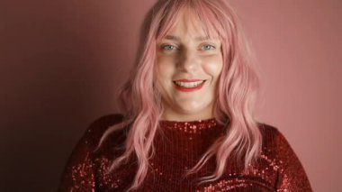 Kırmızı elbise giyen güzel bir kadın pembe arka planda baston şekerlerle kalp yapıyor. Noel kutlaması. Yüksek kaliteli FullHD görüntüler