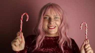 Beyaz elbiseli güzel bir kadının portresi. El kol hareketleri, kalp şeklinde, baston şekerlerle pembe arka planda poz veriyor. Sevgililer Günü. Yüksek kaliteli FullHD görüntüler