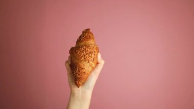 Üniformalı genç kadın fırıncı elinde taze pişmiş altın kruvasan tutuyor. Önlüklü şef pembe arka planda pasta tutuyor. Yüksek kaliteli FullHD görüntüler