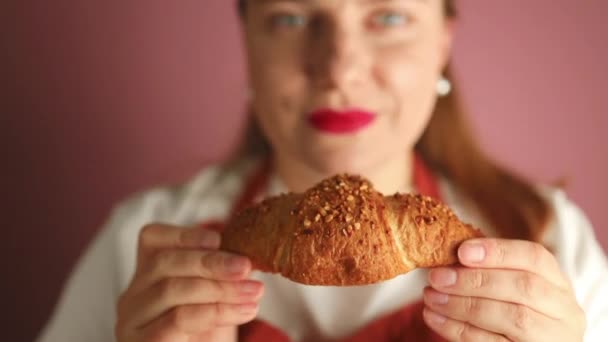 身穿制服的年轻女面包师拿着刚烤好的脆皮的金羊角面包 围裙厨师拿着粉色背景的糕点 优质Fullhd影片 — 图库视频影像