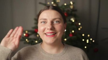 Mutlu gülümseyen beyaz bir kadın kameraya bakıyor ve evdeki Noel ağacının yanında internetten sohbet ediyor. Yüksek kaliteli FullHD görüntüler