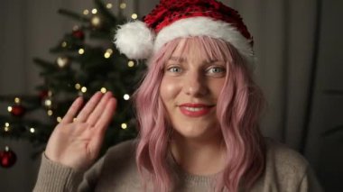 Mutlu gülümseyen beyaz bir kadın kameraya bakıyor ve evdeki Noel ağacının yanında internetten sohbet ediyor. Yüksek kaliteli FullHD görüntüler