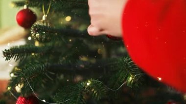 2024 'te, sakin bir kış akşamı, Noel' de ve yeni yılda evdeki şenlik ışıklarının arka planında, Noel ağacını mücevherlerle süsleyen bir kadın görülüyor. Yüksek kaliteli FullHD görüntüler