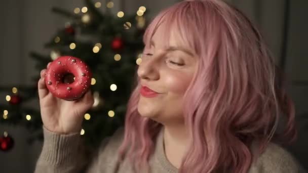 Щаслива Жінка Кусає Пончик Десерт Виглядає Камерою Фоні Різдвяних Вогнів — стокове відео