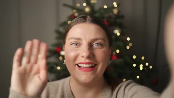 ハッピー笑顔コーカサス美しい女性は 自宅のクリスマスツリーの横のオンラインビデオ通話でカメラを見て笑顔とチャット 高品質のフルHd映像 — ストック動画