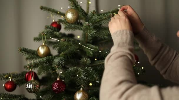 2024 落ち着いた冬の夜 クリスマス 新年にお祝いのライトの背景にクリスマスツリーを飾る女性の手のクローズアップ 高品質のフルHd映像 — ストック動画