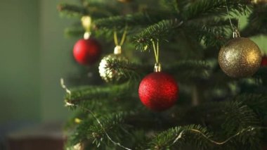 2024 'te, sakin bir kış akşamı, Noel' de ve yeni yılda evdeki şenlik ışıklarının arka planında, Noel ağacını mücevherlerle süsleyen bir kadın görülüyor. Yüksek kaliteli FullHD görüntüler