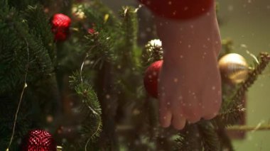 2024 'te, sakin bir kış akşamı, Noel' de ve yeni yılda evdeki şenlik ışıklarının arka planında, Noel ağacını mücevherlerle süsleyen bir kadın görülüyor. Yüksek kaliteli FullHD görüntüler